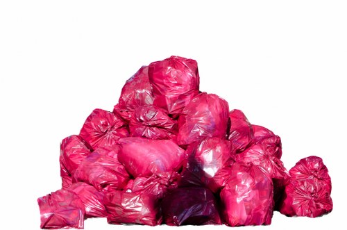 A stack of multiple bright pink rubbish bags made of shiny plastic, piled on top of each other, with some bags leaning against one another, placed outdoors on a flat surface. The bags appear to be filled with garden or household waste, showing some uneven shapes and creases on their surfaces. The environment is well-lit, with no visible background or surroundings in the image. The scene exemplifies waste collection or clearance activities typical of rubbish removal services in the Chigwell area, as provided by Garden Clearance Chigwell, illustrating the typical presentation of bags ready for disposal or collection.
