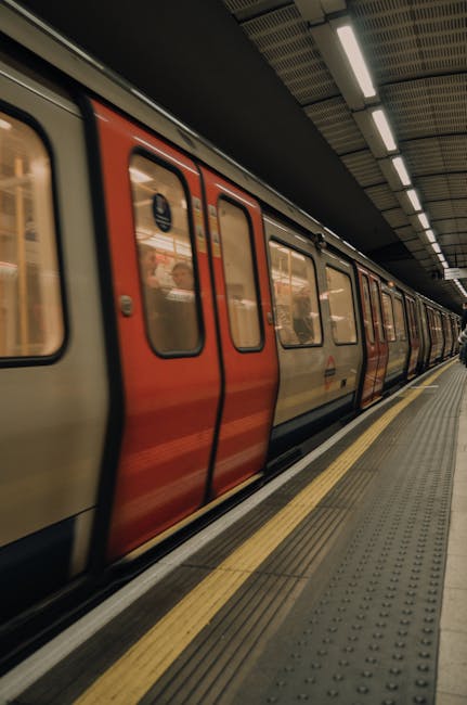 The image depicts an underground London Tube station, viewed from ground level at the edge of a subway platform, looking towards the curved tunnel opening in the distance. The platform surface feature